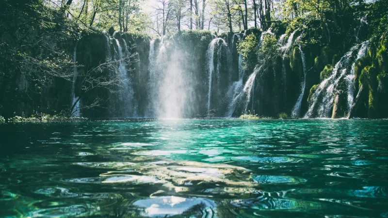 Una hermosa cascada de múltiples niveles que cae en un lago turquesa rodeado de un exuberante bosque verde.